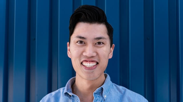 Close up photo of a smiling man with dark hair on a blue.